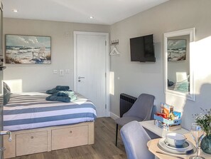 Ein Schlafzimmer mit einem Bett, einem Sessel, einem Tisch mit Schüssel und Weinglas sowie einem Fernseher an der Wand.