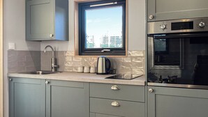 Una cocina moderna con armarios grises, un lavamanos de acero inoxidable, una tetera y una ventana con vistas a la ciudad.