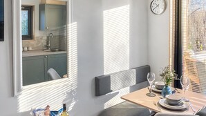 Una cocina moderna con ventana, un comedor con mesa dispuesta para dos personas y un reloj en la pared.