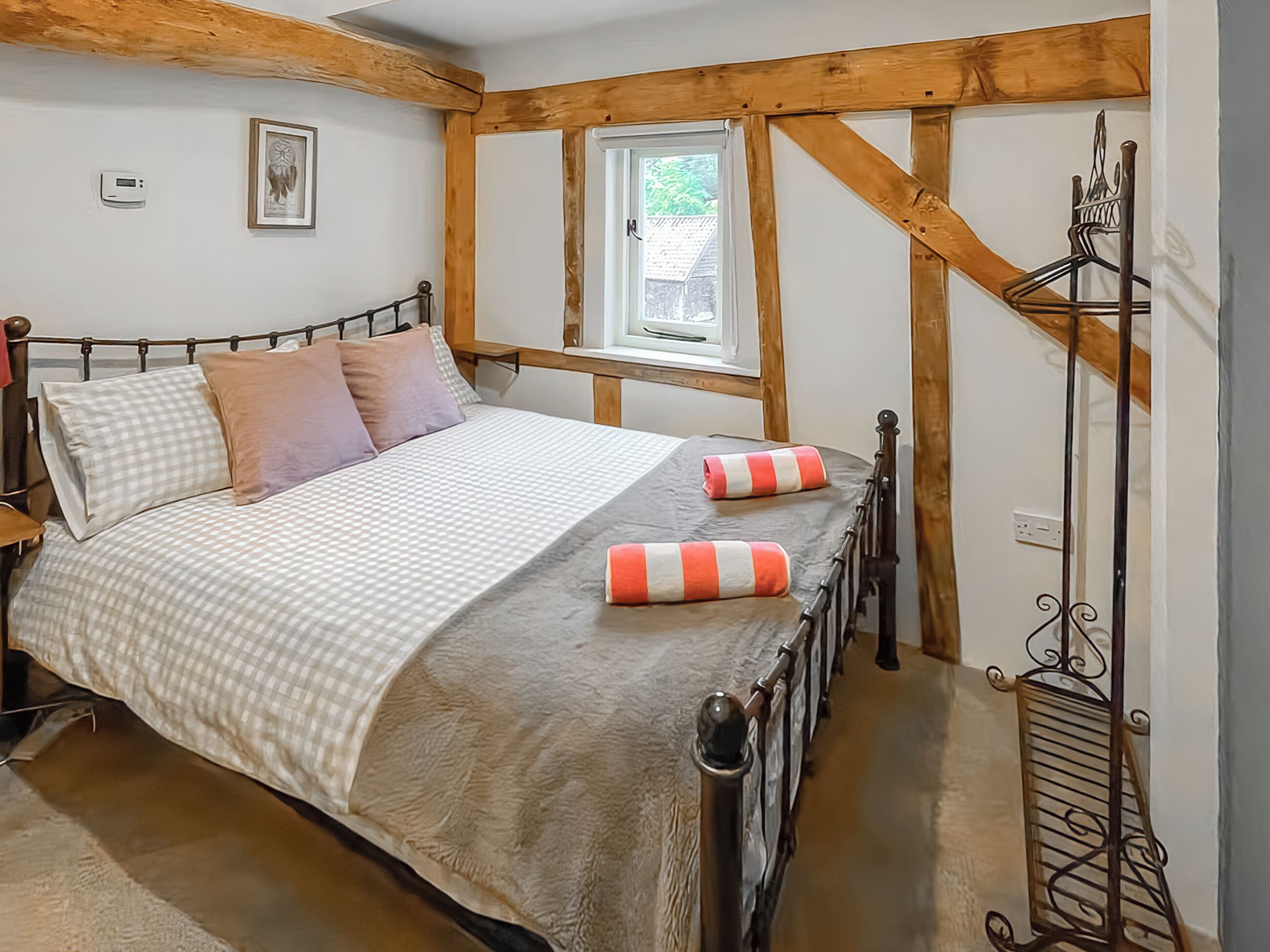 Une chambre à coucher avec un lit, des poutres en bois, une fenêtre et un porte-manteau.