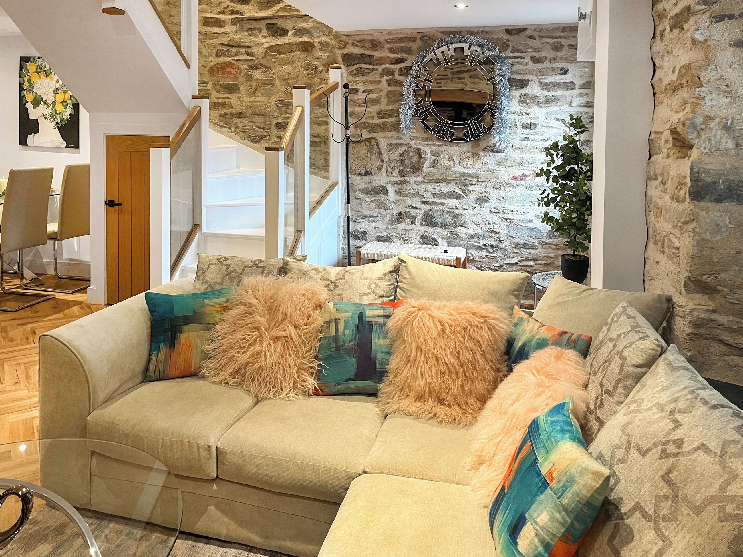 A living room with a stone wall, a wooden staircase, and a sofa with colorful cushions.