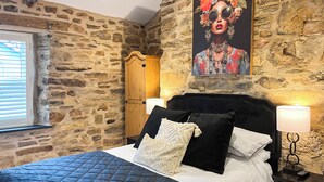 Ein Schlafzimmer mit Steinwand, einem Bett mit schwarzem Kopfteil und einem Holzschrank.