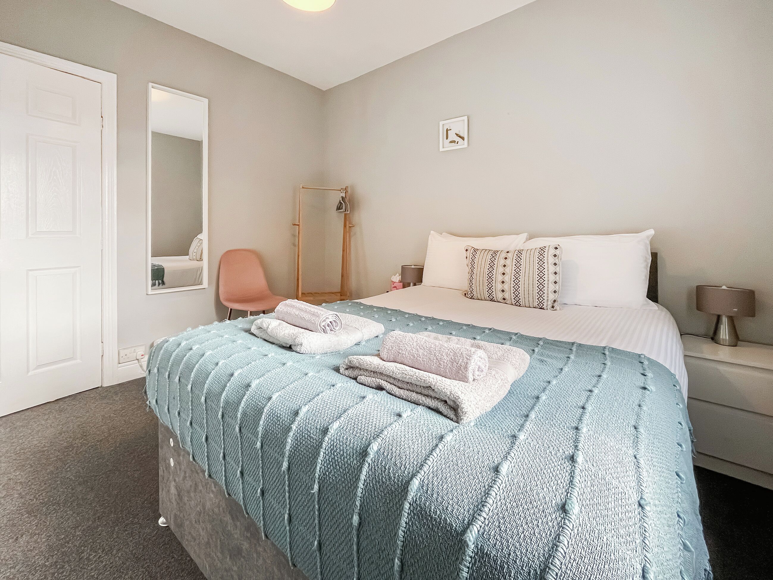 Une chambre à coucher avec un lit, une chaise, un miroir, une table de chevet et une lampe.