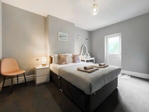 Een slaapkamer met een bed, nachtkastje, stoel en een raam.