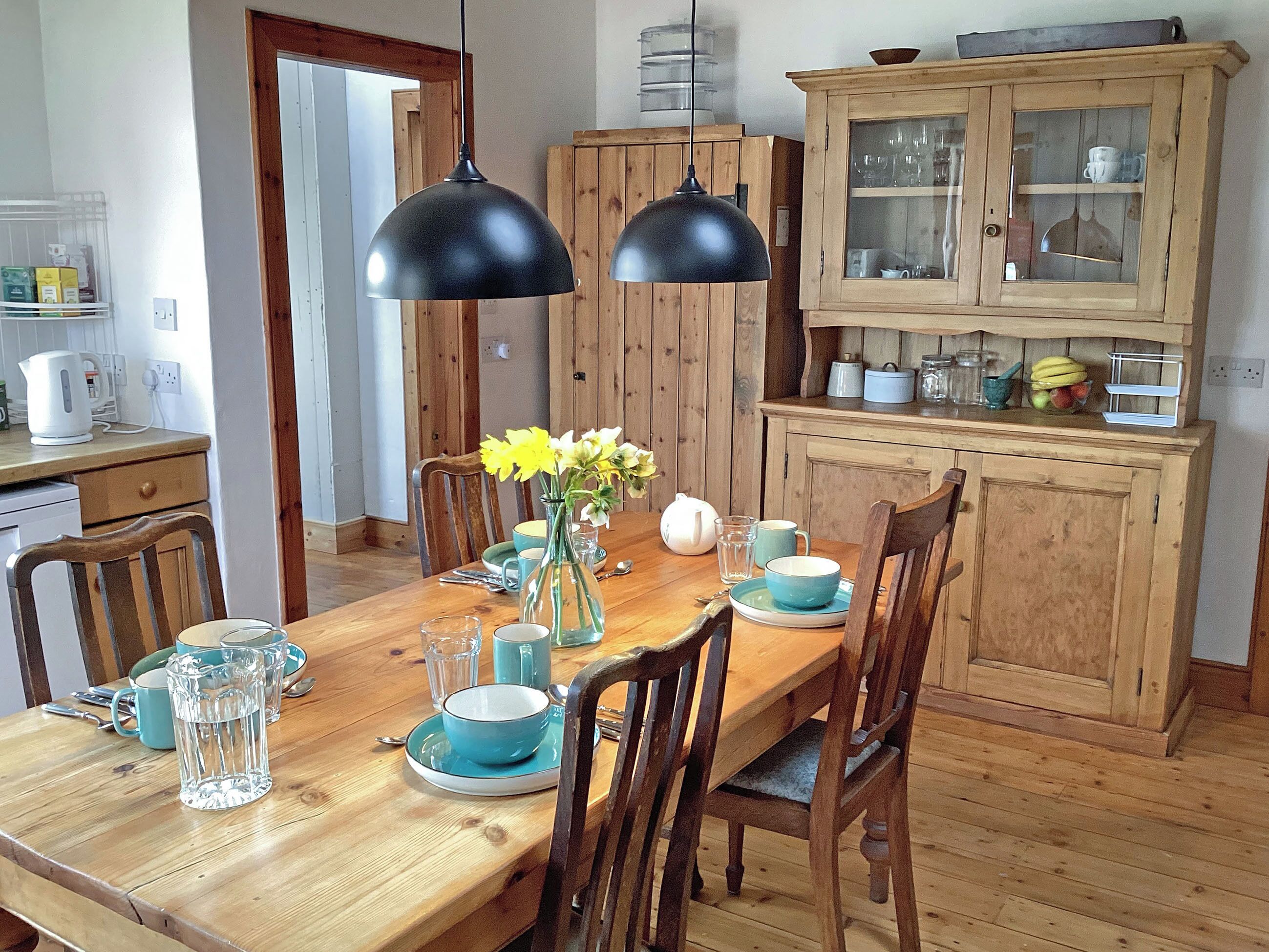 A wooden dining table with chairs, a vase with flowers, and a cabinet with glass doors.