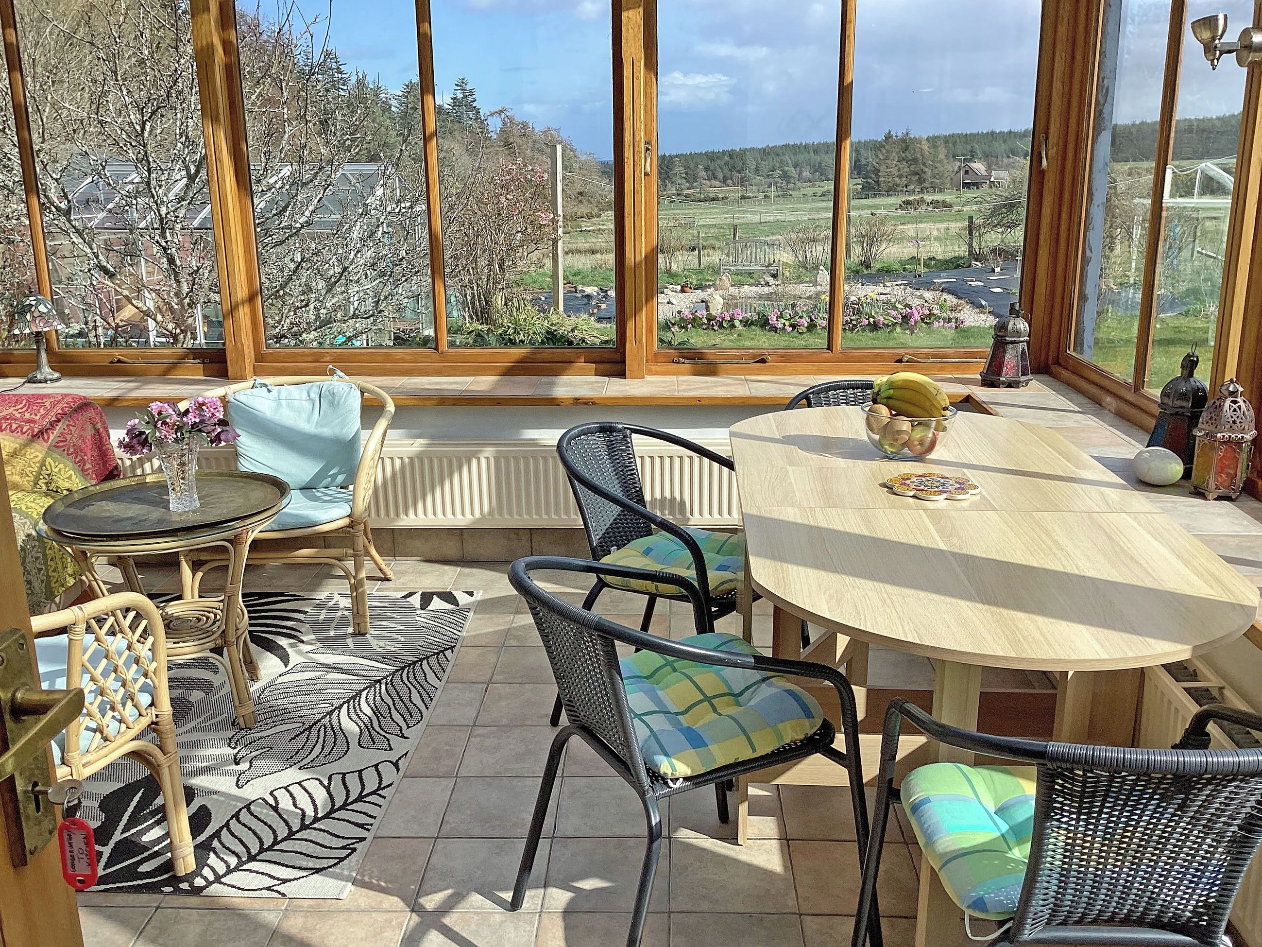 A sunlit patio with wicker furniture, a round table, and a view of a rural landscape.