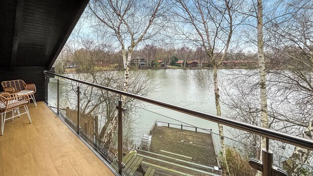 Un balcón con vistas a un lago, piso de madera y mobiliario exterior.