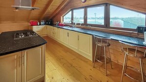 Una cocina con armarios de madera, encimera negra, estufa a gas, ventana con vistas y dos taburetes de bar.