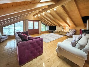 Ein Dachzimmer mit Holzbalkendecke, einem großen Fenster, einem Fernseher und zwei Sofas.