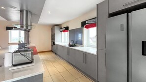 Una cocina moderna con armarios grises, una campana extractora de acero inoxidable y un ventanal con un visillo rojo.