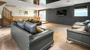 Una sala moderna con sofás de cuero, un televisor de pantalla plana y una escalera.