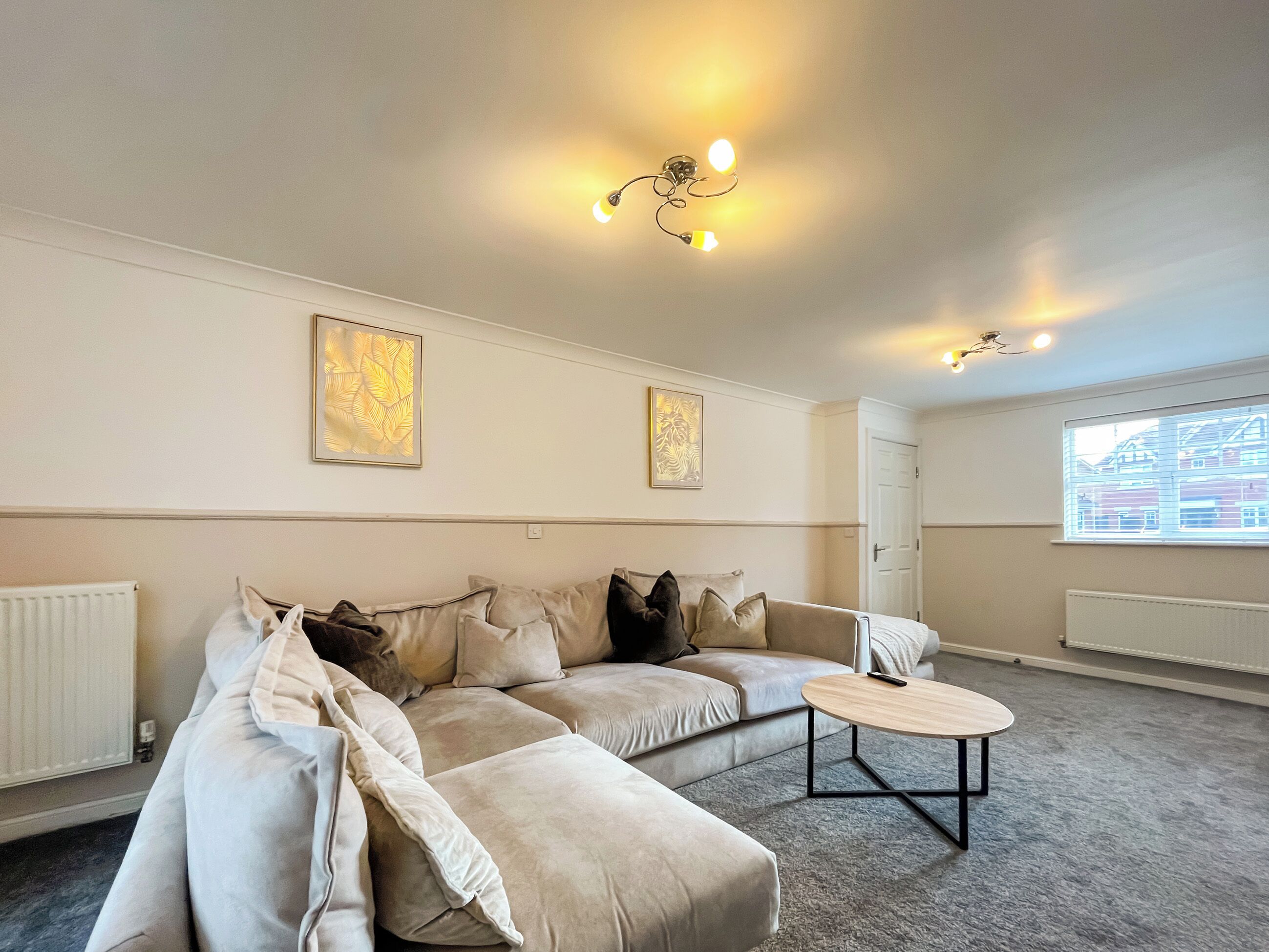 A modern living room with a beige sectional sofa, a round coffee table, and two wall-mounted light fixtures.
