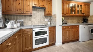 Una cocina con armarios de madera, horno empotrado, lavadora y salpicadero de azulejos.