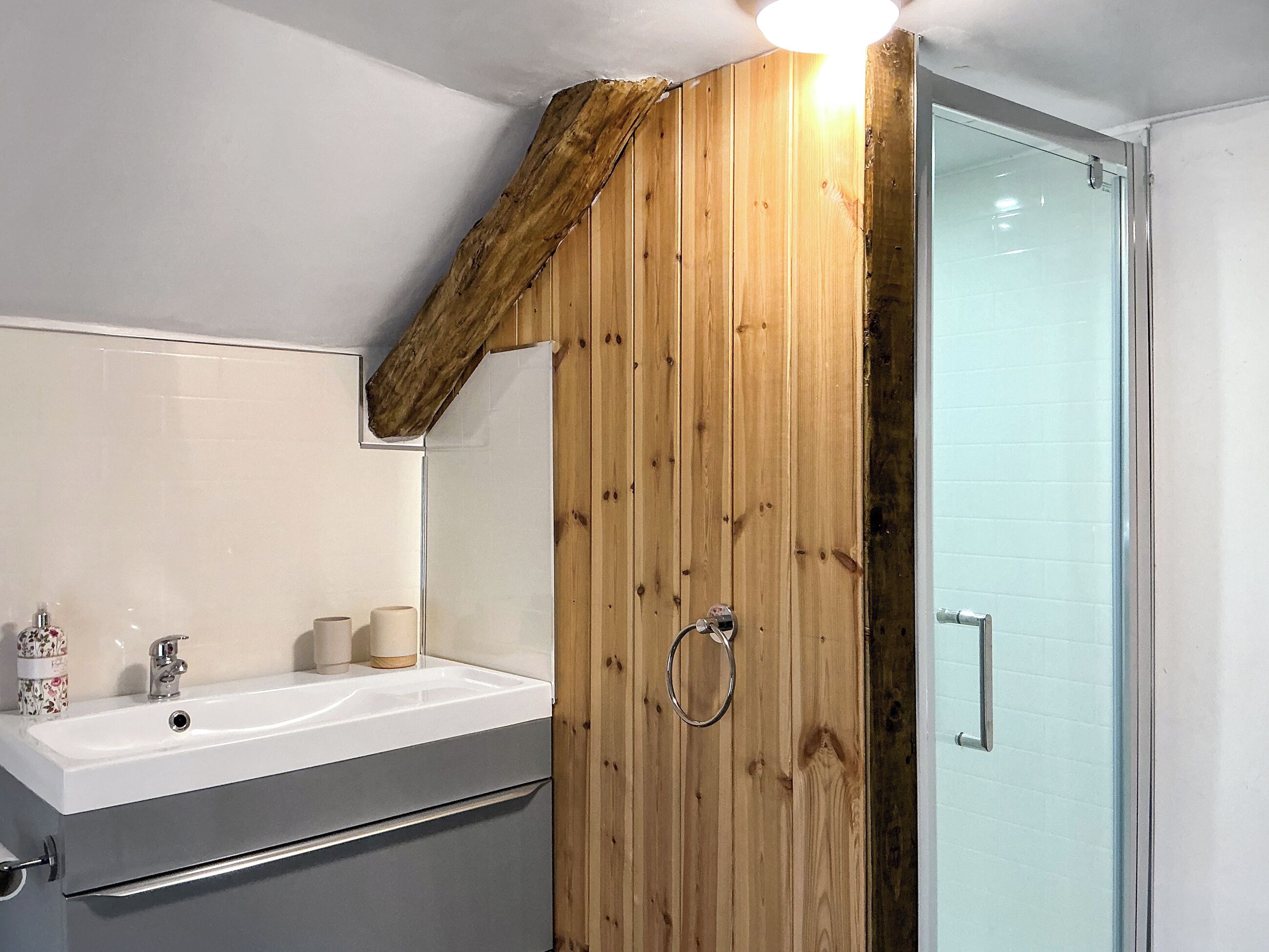A bathroom with a wooden wall, a white sink, and a glass shower door.
