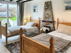 A bedroom with two wooden beds, a stone fireplace, and a view of the outdoors. - 2 bedroom accommodation in North Cornwall (North Cornwall)