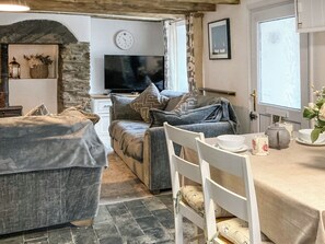 A cozy living room with a stone archway, a television, a sofa, and a dining area with a table and chairs. - 2 bedroom accommodation in North Cornwall (North Cornwall)