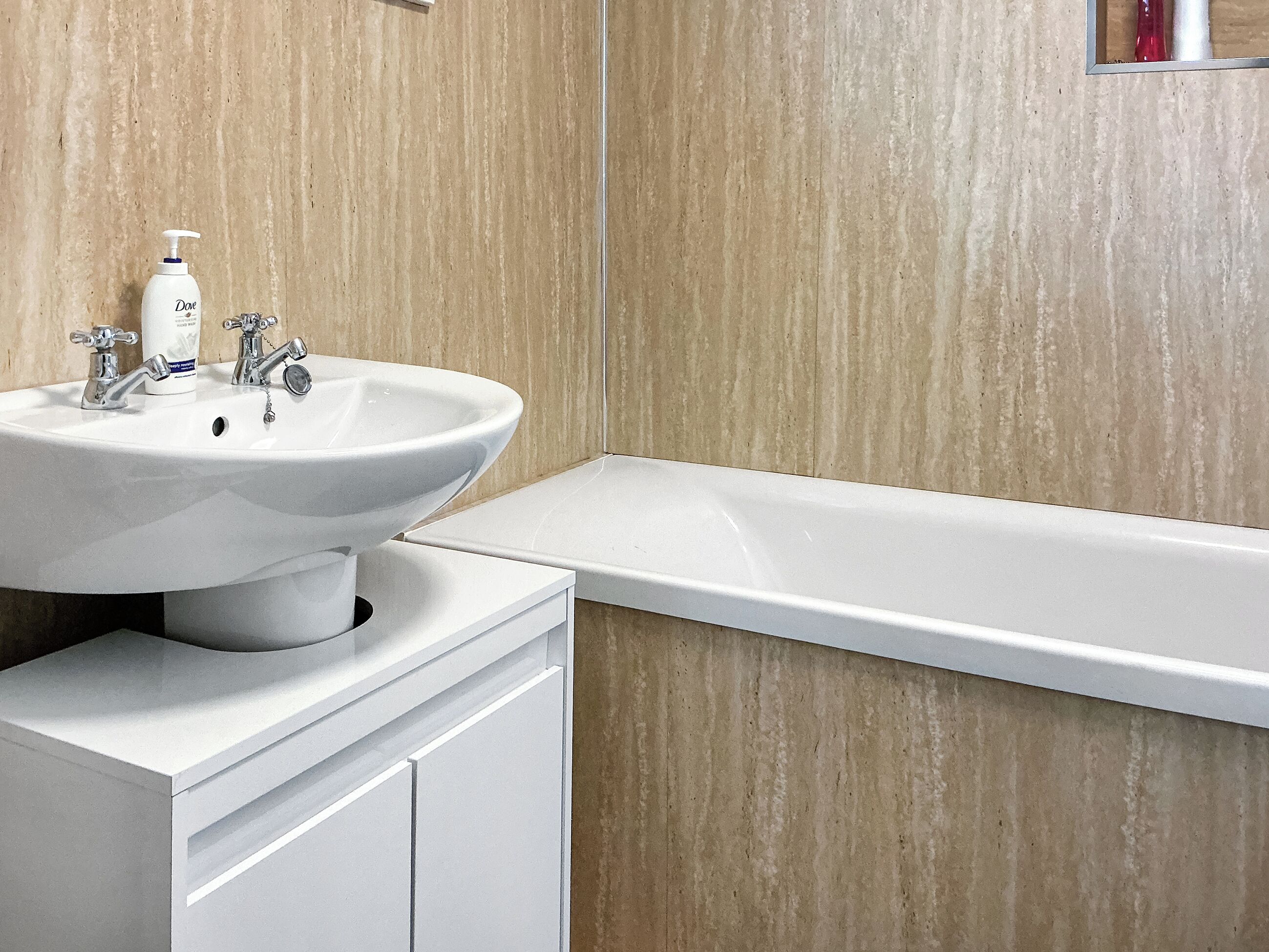 Un bany amb un lavabo blanc, dues aigües, una ampolla de sabó Dove i una banyera blanca.