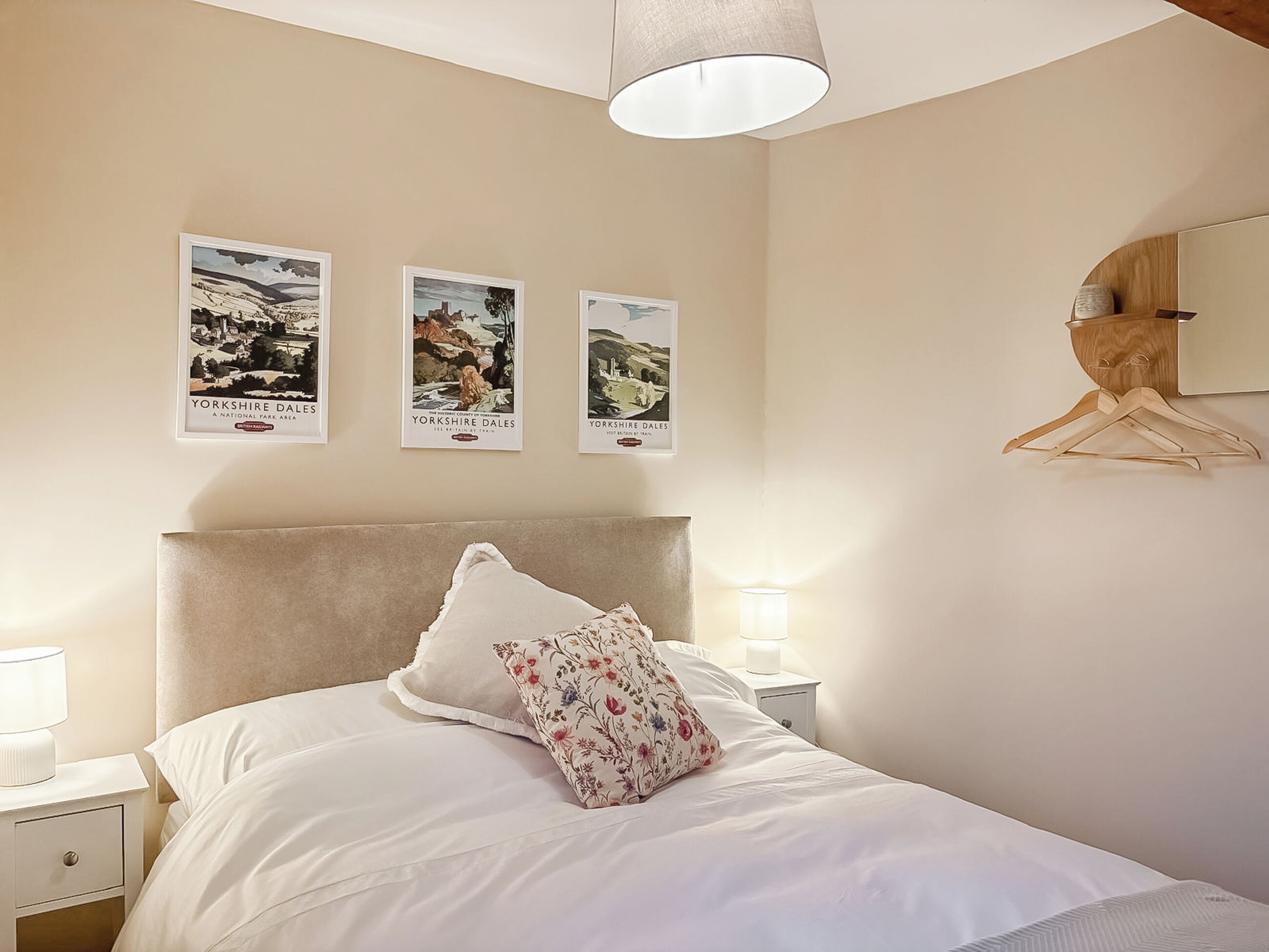 A bedroom with a bed, a nightstand, a lamp, a hanging wooden hanger, and three framed pictures on the wall.