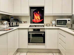 A modern kitchen with white cabinets, a gas stove, a microwave, and a digital clock.