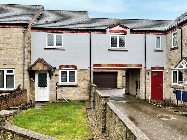 A residential building with a garage, a red door, and a small front yard.