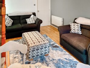 A living room with two sofas, a patterned ottoman, a white chair, and a blue and white patterned rug.