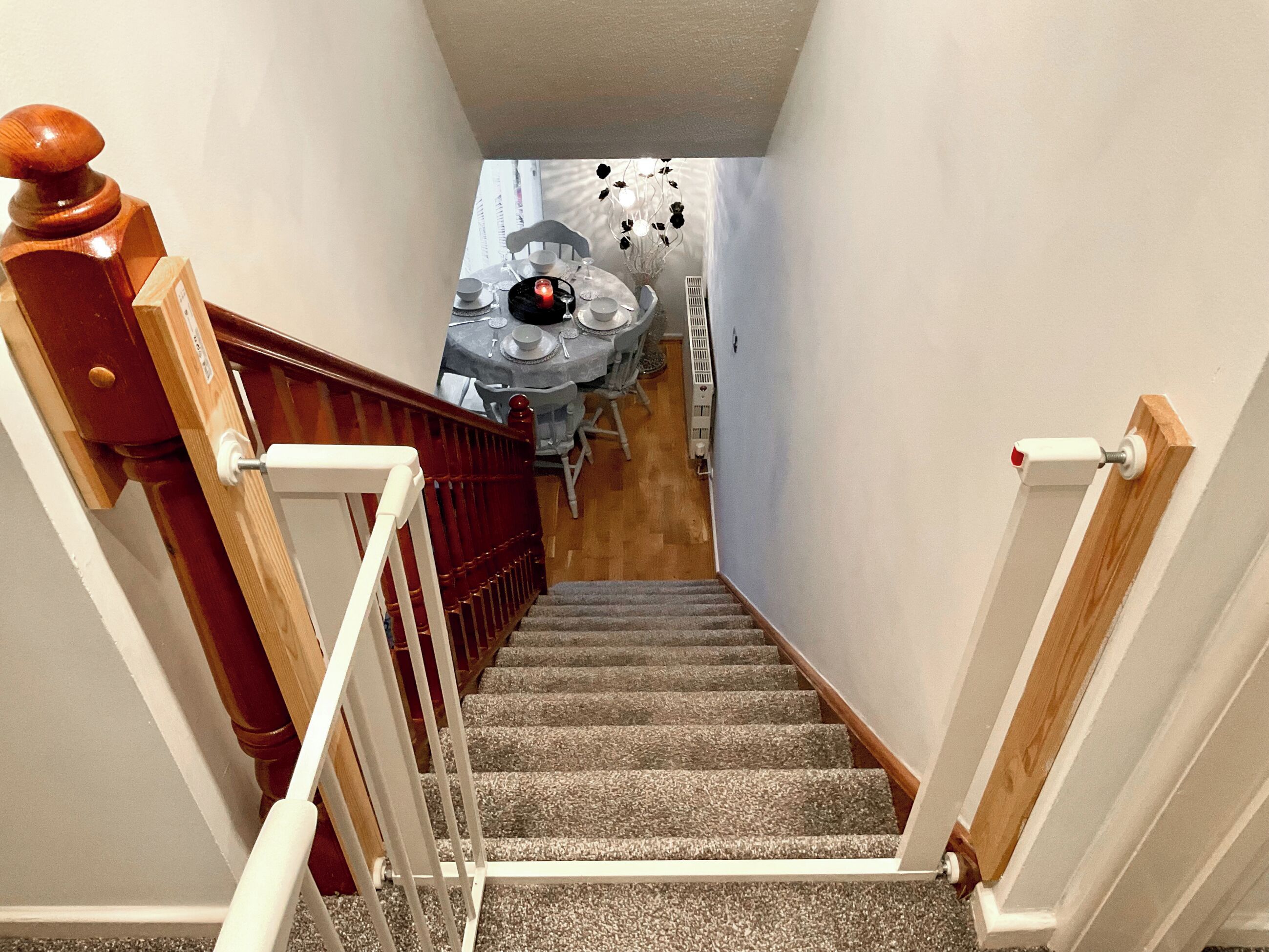 Una escalera conduce a un comedor con una mesa preparada para cuatro personas, una silla y un muro decorativo.