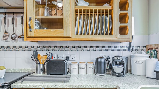 Una cocina con armarios de madera, salpicadero de azulejos y diversos electrodomésticos y utensilios.