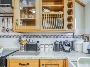 A kitchen with wooden cabinets, a tiled backsplash, and various kitchen appliances and utensils. - 2 bedroom accommodation in Saxmundham (Saxmundham)