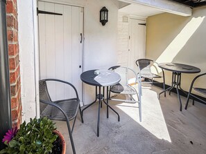 An outdoor patio with a round table and two chairs, a potted plant, and a white door. - 2 bedroom accommodation in Saxmundham (Saxmundham)