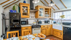 Una cocina con armarios de madera, una mesa de comedor con lo necesario para el desayuno y vistas al exterior a través de una ventana.