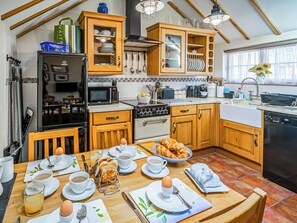 A kitchen with wooden cabinets, a dining table set with breakfast items, and a view of the outdoors through a window. - 2 bedroom accommodation in Saxmundham (Saxmundham)
