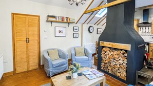 Una sala de estar acogedora con dos sillones azules, una mesa de centro de madera, una chimenea con revestimiento de piedra y una estantería llena de libros.