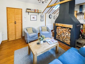 A cozy living room with two blue armchairs, a wooden coffee table, a fireplace with a stone surround, and a bookshelf with books. - 2 bedroom accommodation in Saxmundham (Saxmundham)