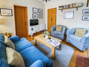 A living room with a sofa, armchair, coffee table, and a bookshelf. - 2 bedroom accommodation in Saxmundham (Saxmundham)