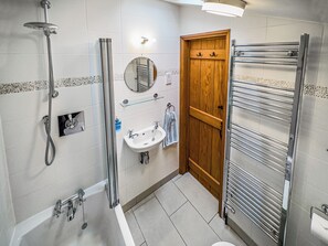 A bathroom with a shower, sink, wooden door, towel rack, and a mirror. - 2 bedroom accommodation in Saxmundham (Saxmundham)