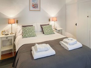 A neatly made bed with two pillows, a bedside table with a lamp, a clock, and a framed picture on the wall. - 2 bedroom accommodation in Saxmundham (Saxmundham)