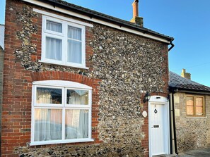 A two-story building with a stone facade, a white door, and a window with curtains. - 1 bedroom accommodation in Saxmundham (Saxmundham)