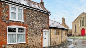 A stone building with a red door, a white window, and a brick wall. - 1 bedroom accommodation in Saxmundham (Saxmundham)