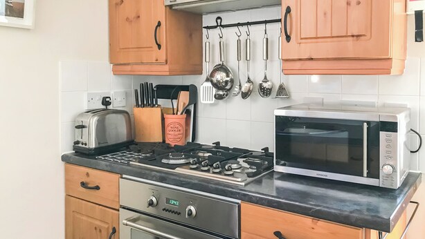 A kitchen with a stove, oven, microwave, and a hanging utensil rack. - 1 bedroom accommodation in Saxmundham (Saxmundham)