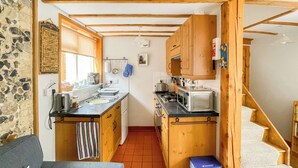 A compact kitchen with wooden cabinets, a stove, a microwave, and a sink. - 1 bedroom accommodation in Saxmundham (Saxmundham)