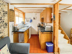 A compact kitchen with wooden cabinets, a stove, a microwave, and a sink. - 1 bedroom accommodation in Saxmundham (Saxmundham)