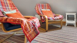 Deux fauteuils confortables avec des couvertures colorées, un petit radiateur blanc et une fenêtre laissant entrer la lumière naturelle.