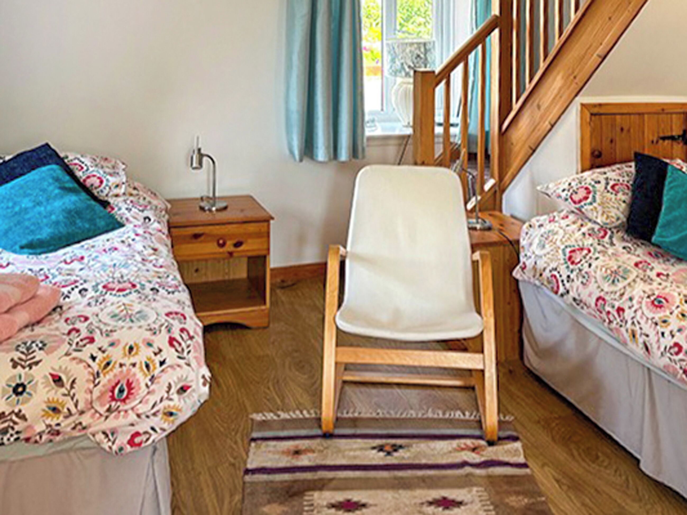 Een slaapkamer met twee bedden, een houten stoel, een nachtkastje en een raam met gordijnen.