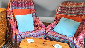 Deux fauteuils à motifs avec des coussins bleus, une table en bois et une commode à tiroirs.