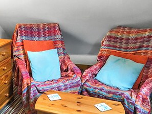 Zwei gemusterte Sessel mit blauen Kissen, ein Holztisch und eine Kommode mit Schubladen.