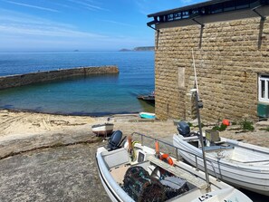 A stone building with a view of the sea, a dock with boats, and a sandy beach. - Escape to something special, surrounded by peaceful countryside. (St Just)