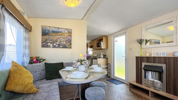 Een gezellige eethoek met een tafel voor vier personen, een bank met kussens, een schilderij aan de muur en een open haard.