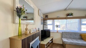 Een woonkamer met een open haard, een televisie, een bank en een raam met uitzicht op het omliggende landschap.