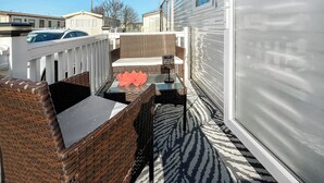 Een klein terras buiten met rieten meubels, een glazen tafel en een vloerkleed met dessin.