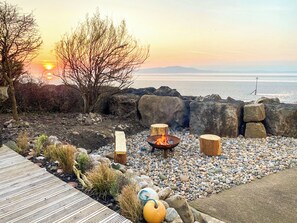 Eine Terrasse mit Feuerstelle, Sitzgelegenheiten und Blick auf den Ozean bei Sonnenuntergang.